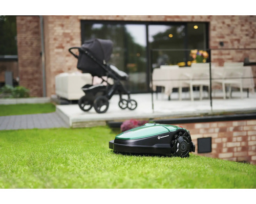 Rasenmähroboter auf einer Rasenfläche, im Hintergrund ein Kinderwagen und ein Haus.