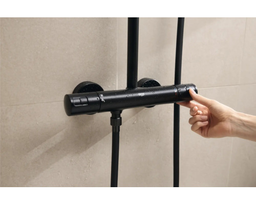 Schwarzer Duschthermostat mit Bedienung durch eine Hand vor gefliester Wand