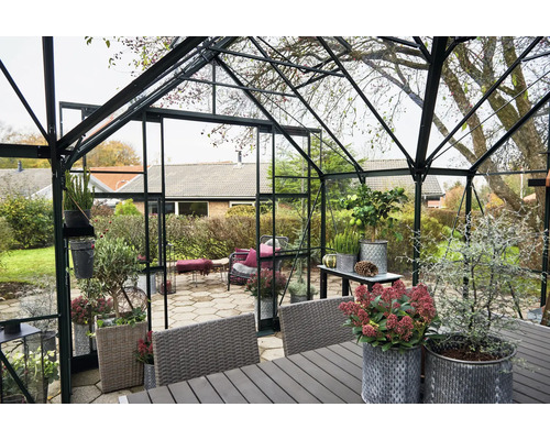 Gewächshaus mit Pflanzen und Gartenmöbeln in einem Garten.