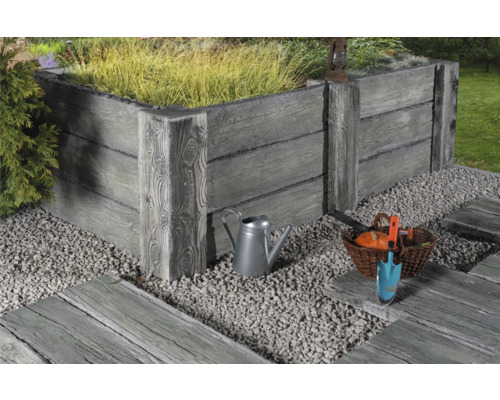Hochbeet aus Beton mit Holzoptik, umgeben von Kies und Gartenwerkzeugen