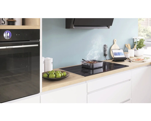 Moderne Küche mit Einbaubackofen, Kochfeld, Dunstabzugshaube und Kochutensilien auf der Arbeitsplatte.