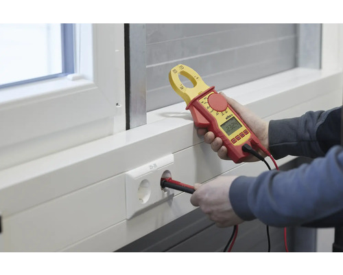 Elektriker misst Spannung an einer Steckdose mit einem Strommessgerät