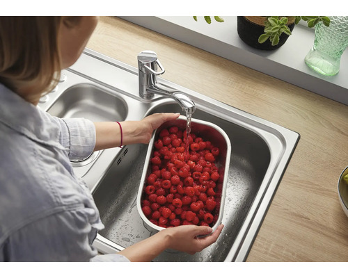 Frau wäscht Himbeeren in Edelstahlschale unter Wasserhahn in Edelstahlspüle