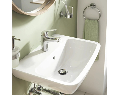 Waschbecken mit Armatur, Spiegel und Badaccessoires in einem Badezimmer.