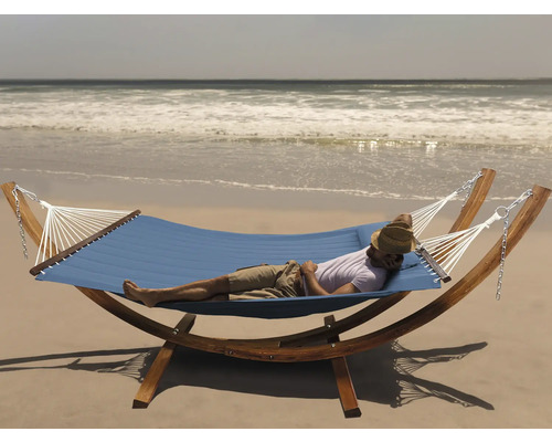 Mann entspannt in einer blauen Hängematte mit Holzgestell am Strand