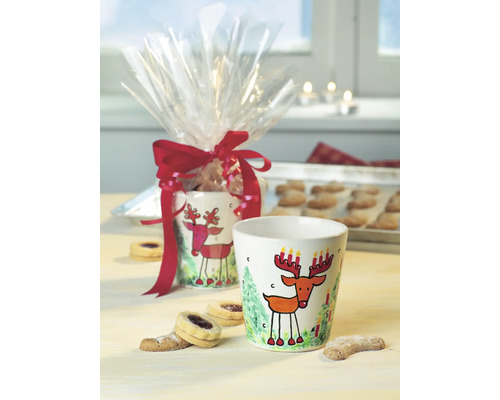 Dekorativer Becher mit Rentier Motiv und Geschenkverpackung auf einem Tisch mit Keksen.