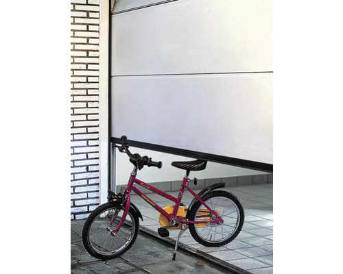 Eine teilweise geöffnete weiße Garagentor mit einem Kinderfahrrad davor.