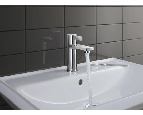 Waschbeckenarmatur aus Metall mit Wasserstrahl auf weißem Waschbecken