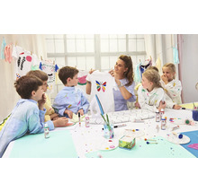 Gruppe von Kindern und eine Frau verzieren T-Shirts mit Textilfarbe an einem Tisch.