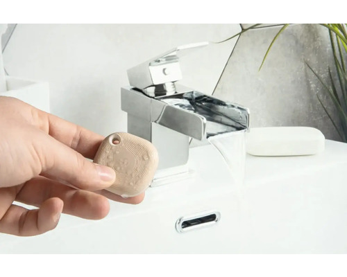 Eine Person hält einen Aromastein vor einem Wasserhahn im Badezimmer