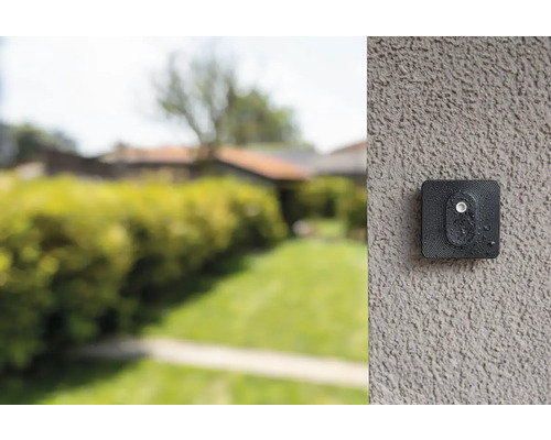 Überwachungskamera an einer Wand mit Garten im Hintergrund