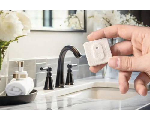 Hand hält einen Wassermelder im Badezimmer mit Waschbecken und Armatur