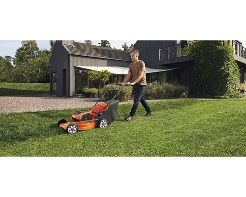 Mann mäht Rasen mit einem Rasenmäher der Marke Husqvarna in einem Garten vor einem Haus.