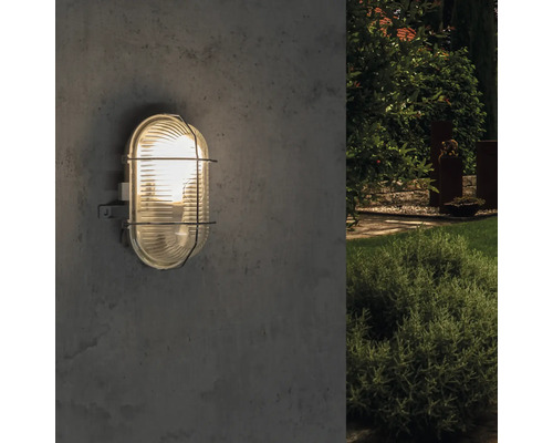 Oval geformte Aussenleuchte mit Schutzgitter an einer Wand montiert.