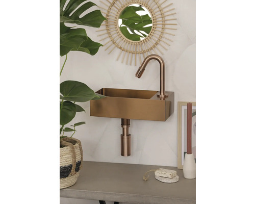 Wandmontiertes Waschbecken aus Metall mit Armatur in einem Badezimmer mit Spiegel und Pflanze.