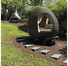 Gartenszene mit einem runden, überdachten Outdoor-Bett und einer Hängematte auf einem grünen Hügel