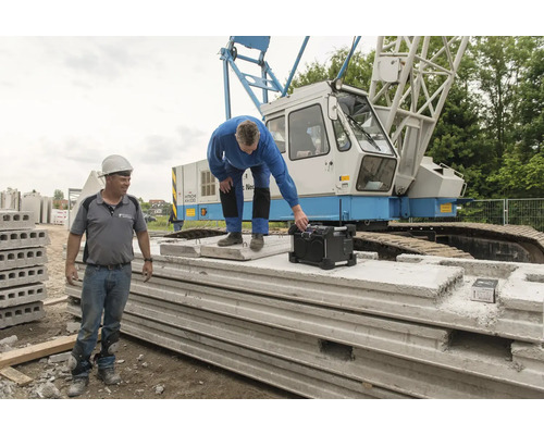 Zwei Bauarbeiter mit Baustellenradio und Betonfertigteilen vor einem Kran