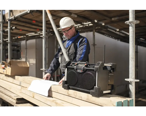 Baustellenradio mit Bauarbeiter beim Blick auf Baupläne