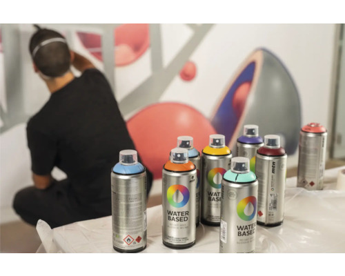 Mehrere Farbspraydosen von Montana vor einer Wand mit einem sich entfernenden Mann.