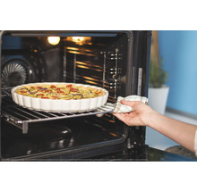 Ein offener Backofen zeigt eine Quiche in einer weißen Form auf einem Gitterrost, die von einer Hand mit einem Ofenhandschuh hineingeschoben wird.