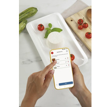 Eine Person benutzt eine App zur Rezeptauswahl mit Zutaten neben einem Teller mit Ricotta, Tomaten, Basilikum und Zucchini.