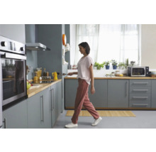 Helle Küche mit Einbaubackofen, Dunstabzugshaube und Frau mit Pfanne.