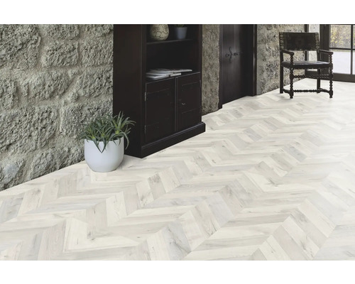 Heller Raum mit Parkettboden im Fischgrätmuster, Steintreppe und dunklem Holzschrank.