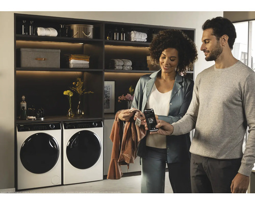 Waschmaschinen und Regale in einem hellen Raum mit einem Paar, das ein Mobiltelefon betrachtet