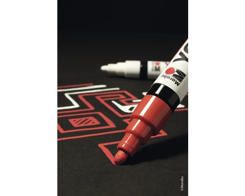 Ein roter Lackmarker zeichnet eine Linie auf schwarzem Papier. Ein weiterer Marker liegt im Hintergrund.