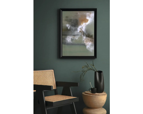 Szene mit einem gerahmten abstrakten Kunstwerk, einem Rattansessel und einem Beistelltisch mit Dekoration.