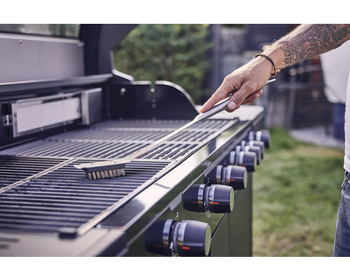 Eine Person reinigt einen Grillrost mit einer Grillbürste.