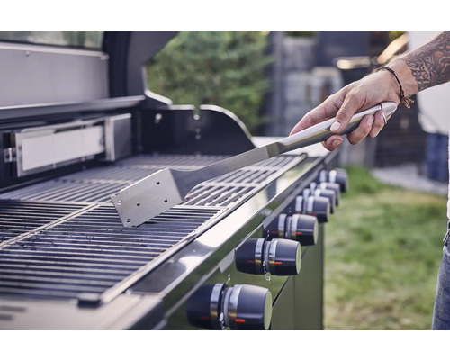 Eine Person reinigt einen Grillrost mit einem Grillspatel.
