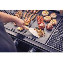 Essenszubereitung auf einem Grill mit Grillwender, Würstchen, Gemüse, Tomaten und gefüllten Champignons.