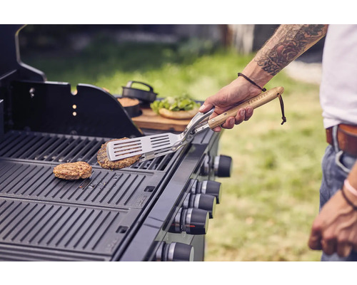 Person wendet Burger auf einem Gasgrill mit Grillbesteck