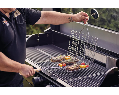 Person grillt Steaks und Gemüse mit einem Grillkorb auf einem Gasgrill.