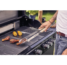 Mann grillt Hähnchenkeulen und Maiskolben mit einer Grillzange auf einem Grill