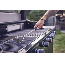 Eine Person reinigt mit einer Grillbürste einen Grillrost.