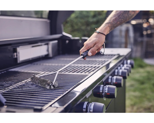 Eine Person reinigt mit einer Grillbürste einen Grillrost.