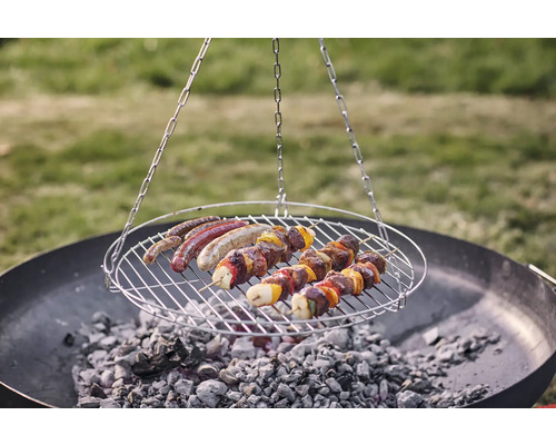 Schwenkgrill mit Würstchen und Fleischspießen über Holzkohle
