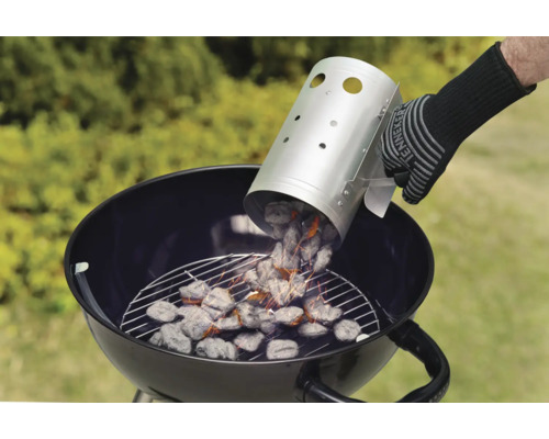 Person gießt Holzkohle aus einem Anzündkamin in einen Kugelgrill.