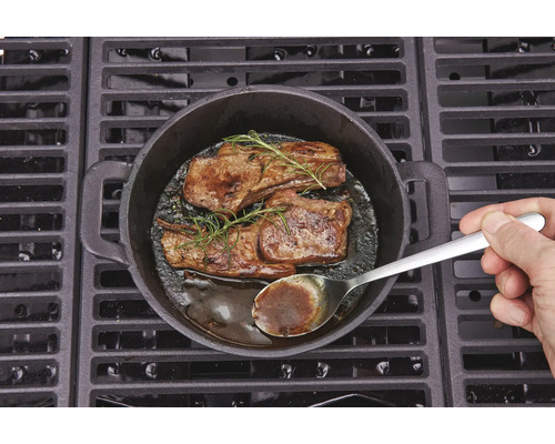 Zwei Steaks mit Rosmarin in einer Gusspfanne auf einem Grill zubereitet