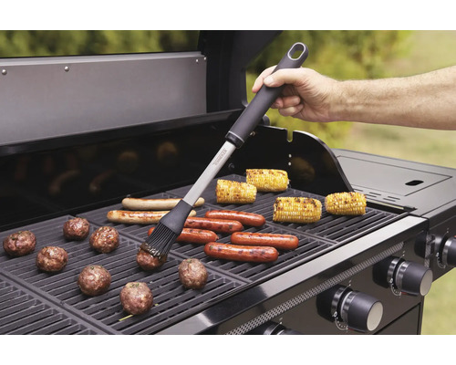 Grillszene mit Grillbürste, Würstchen, Maiskolben und Fleischbällchen auf einem Gasgrill.