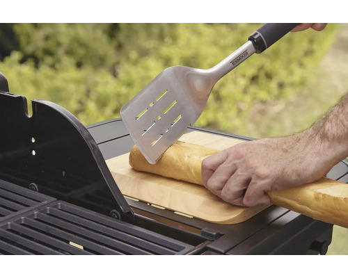 Eine Person schneidet ein Baguette mit einem Grillwender auf einem Grill.