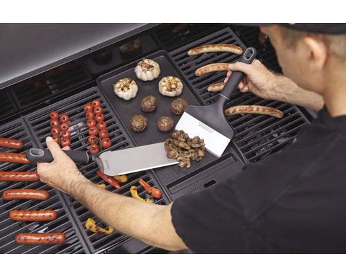 Mann grillt Würstchen, Gemüse und Knoblauch auf einem Grill mit Grillwendern.