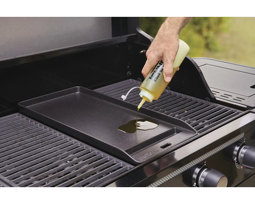 Eine Person gießt Öl auf eine Grillplatte auf einem Gasgrill.