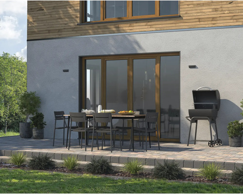 Außenszene mit Grill, Gartentisch und Stühlen auf einer Terrasse vor einem Wohnhaus