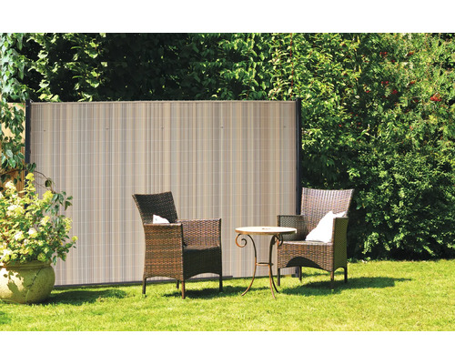 Gartenszene mit Sichtschutzzaun aus Kunststoff, Korbsesseln und kleinem Tisch auf einer Rasenfläche.