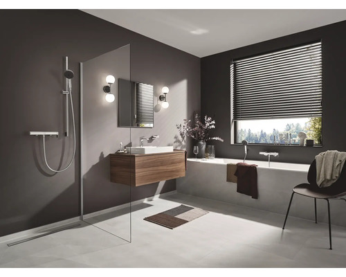 Badezimmer mit Dusche, Waschtisch, Spiegel und Badewanne unter einem Fenster mit Jalousien