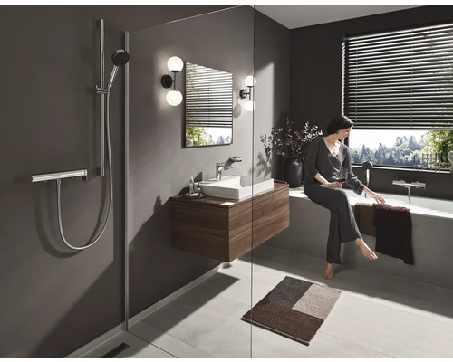 Modernes Badezimmer mit Dusche, Waschtisch, Spiegel, Badewanne und einer Frau, die am Wannenrand sitzt