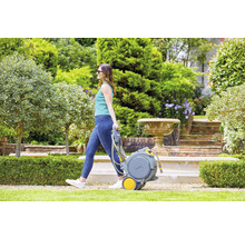 Frau zieht einen Gartenschlauchwagen in einem Garten mit Springbrunnen.